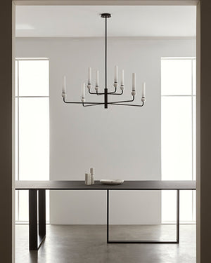 Modern black chandelier hanging above a dining table in a minimalistic room.