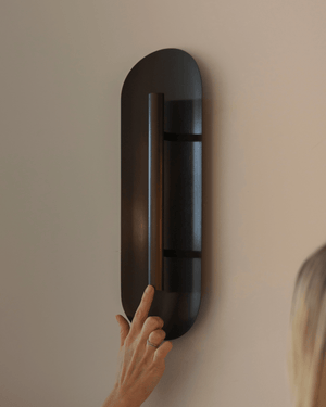 A modern dark bronze wall light on a beige wall