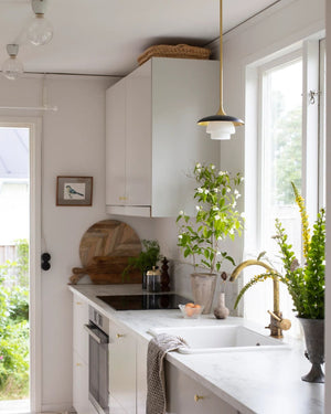 Mid Century Layered Pendant Light suspended above a marble kitchen countertop in a bright white kitchen with plants