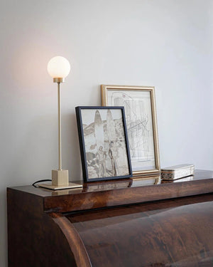Framed artwork and a lMid-Century Modern Orb Table Lamp on a wooden surface against a light gray wall.