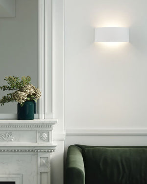White ceramic wall light with wedge profile installed above marble fireplace mantle in a living room