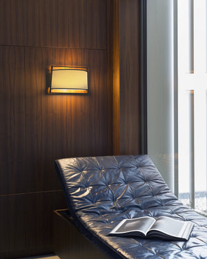 Blue cushioned chair with an open book against a wooden wall with a wall lamp.