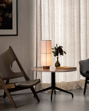 Minimalist Linen Table Lamp Hashira with natural linen shade placed on books within a dark timber bookshelf
