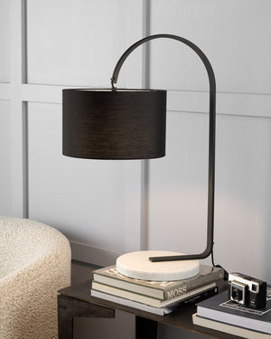 Modern black shade and marble base table lamp on a side table with books and a camera.
