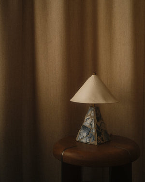 Mosaic ceramic table lamp with blue swirl pattern base and white ribbed shade on wound wooden table