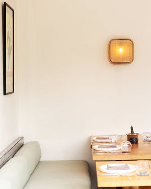 A square shaped natural bagor weave wall light mounted above a restaurant table