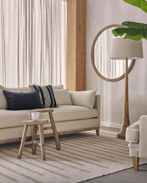 Natural timber floor lamp with linen drum shade styled beside sofa in neutral contemporary living room
