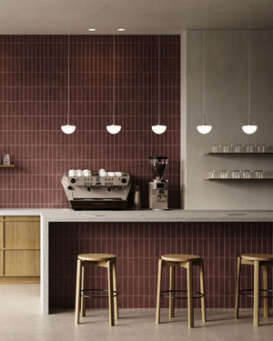 Opal glass dome pendant in a modern kitchen with coffee machine, shelves, and stools against a red tiled wall.