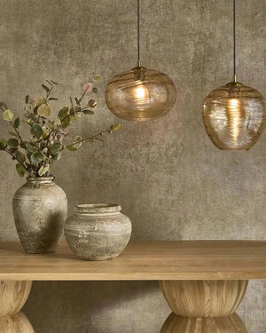 Two hanging glass pendant lights above a wooden table with decorative vases and plants against a textured wall.