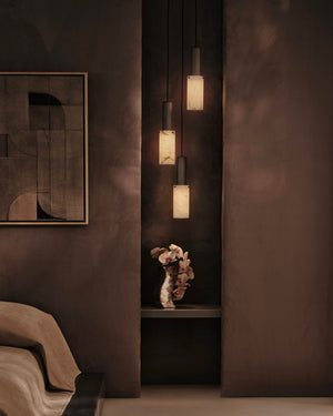 A modern multi-light pendant chandelier with three cylindrical alabaster shades and dark metal frames, hanging in a dark, atmospheric room setting.