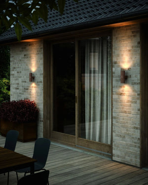Outdoor patio area with brick walls, sliding glass door, and wall-mounted lights at night - Lighting Collective 