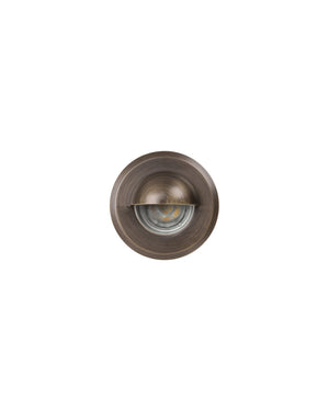 Round eyelid step light in antique brass viewed face on with darkened trim and eyelid shield