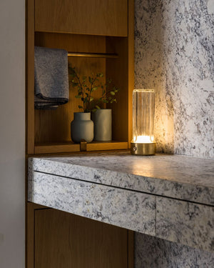 Modern interior with a marble countertop, wooden shelf, and table lamp.
