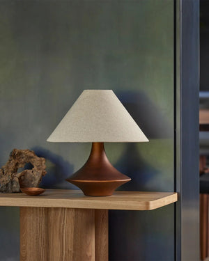 Sculpted bronze ceramic table lamp on oak console styled with natural objects against green plastered wall
