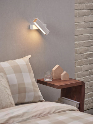 Modern white wall lamp above a bed with a wooden nightstand and decorative items.