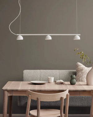 Dining area with wooden table, chairs, and a bench against a dark gray wall with a Simplistic Three Light Rail Pendant 