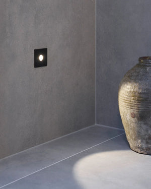 Black modern wall light fixture on a gray concrete wall with a textured vase.