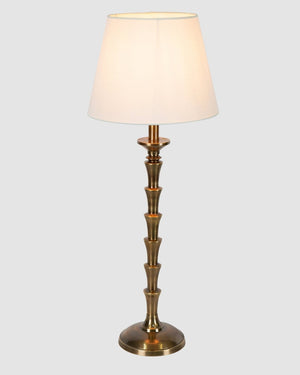 Stacked candlestick table lamp in an antique brass finish with tapered ivory linen shade