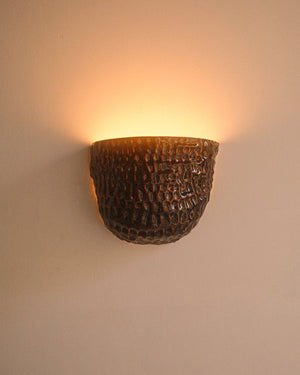 Dark brown pinched ceramic textured sconce mounted on white wall with light on