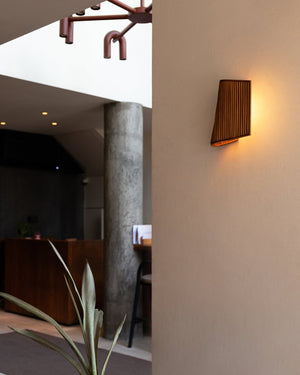 A warm light glowing on a vertical reed wall sconce mounted on a white wall above a plant