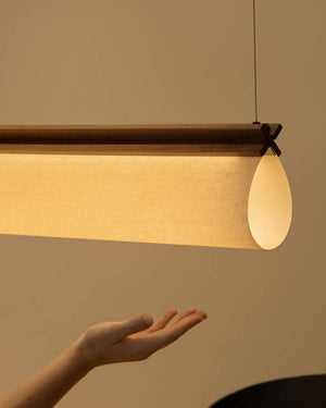 A warmly lit ceiling light with a folded papyrus and a dark timber trim hanging above a hand