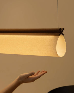 A warmly lit ceiling light with a folded papyrus and a dark timber trim hanging above a hand